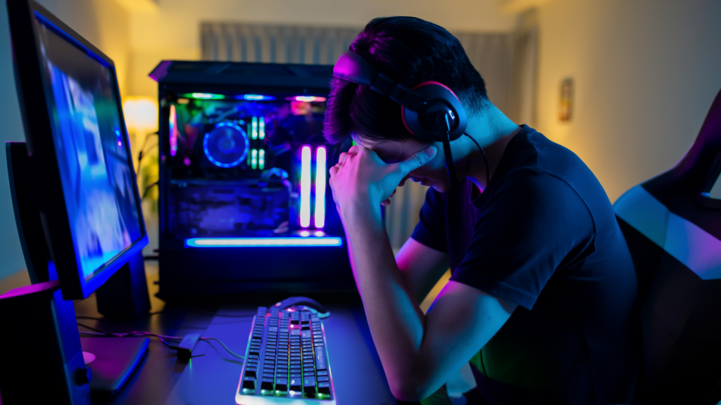 Teenager disappointed at computer desk playing investing game.